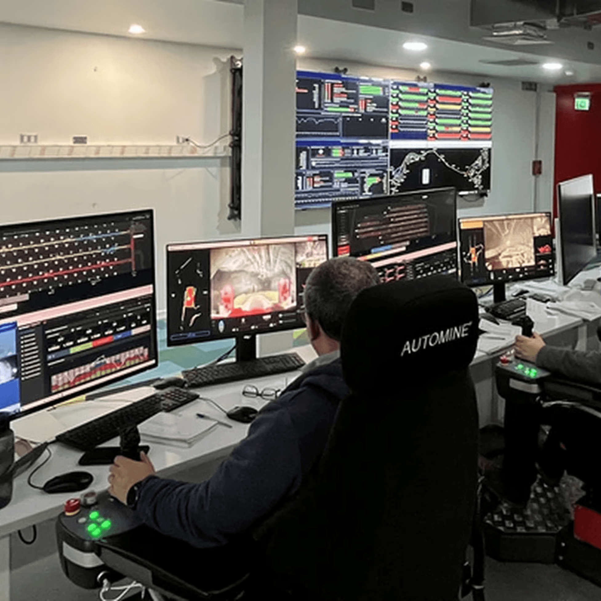 Bogger teleoperator at a surface control station with multiple monitors, joysticks, and CCTV camera feeds